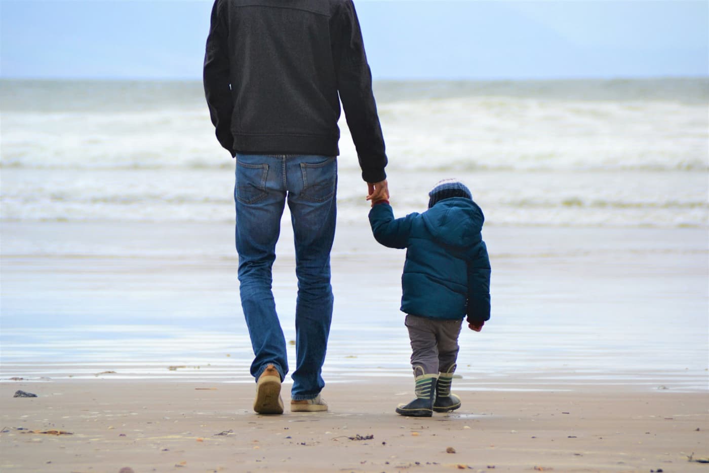 A father and young child walking hand in hand on the beach